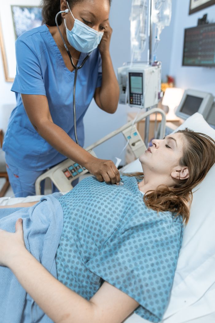 Home A nurse uses a stethoscope to check a female patient lying in a hospital bed.