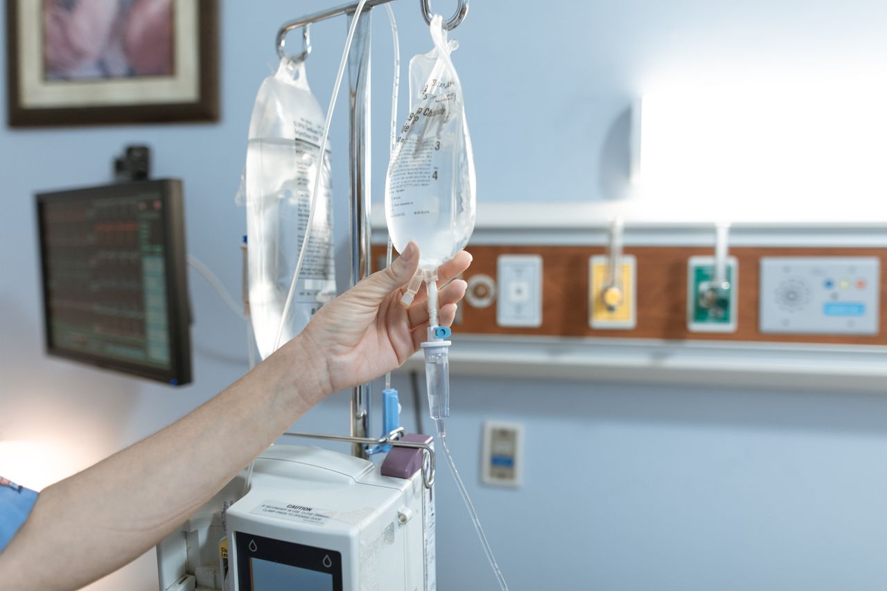 Home Close-up image of an IV drip and hand in a hospital room, illustrating medical care.